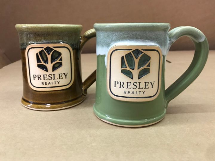 two coffee mugs with the log of a tree and 'presley realty' in text