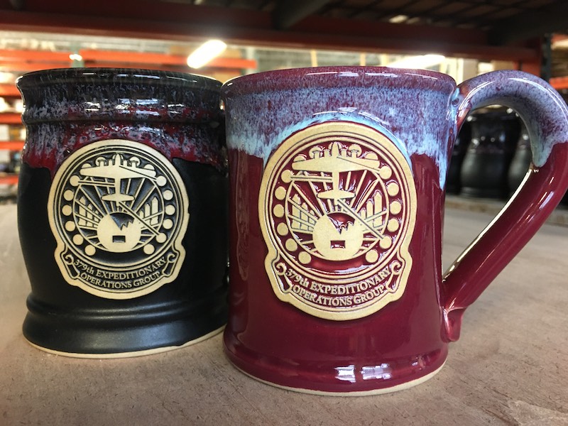 Black and red coffee mugs with military emblems.