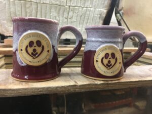 Two red coffee mugs on a kiln with the Text "every child deserves a home" with an illustration of an outline of two people holding a child. 