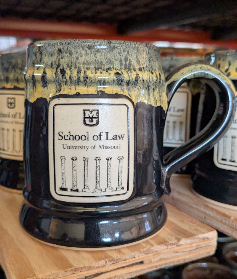 black pottery mug with a school alumni logo in the center