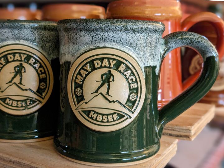 green coffee mugs with a logo of a figure skiing in a may day race