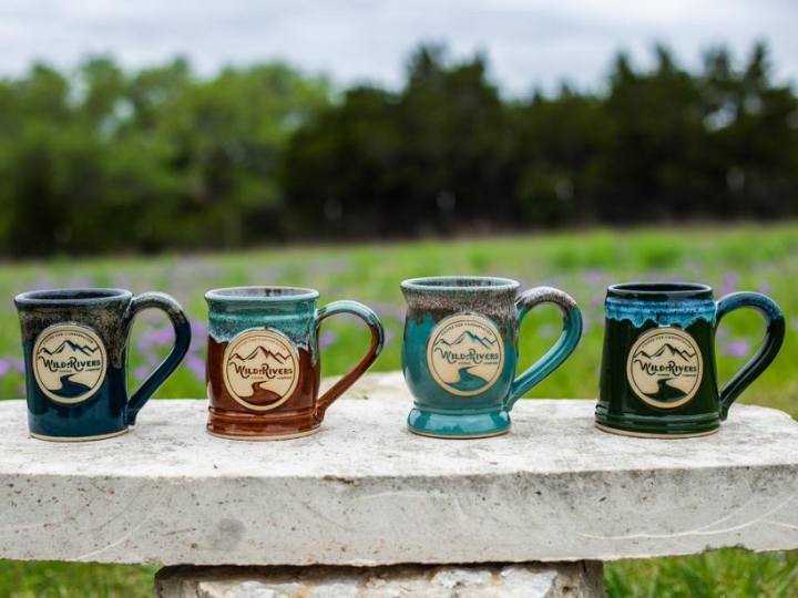 Four coffee mugs with logos sitting on a stone bench with trees in the background.